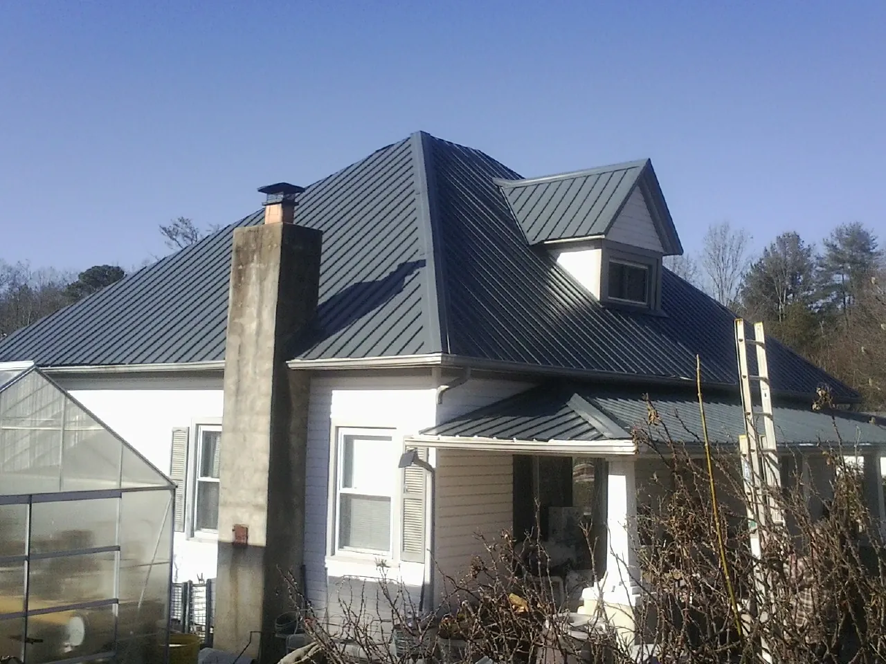 Dark blue standing seam metal roof on a white farmhouse with dormer — Slate & Tile Roof Repair by Roofing Brothers in Hardyville