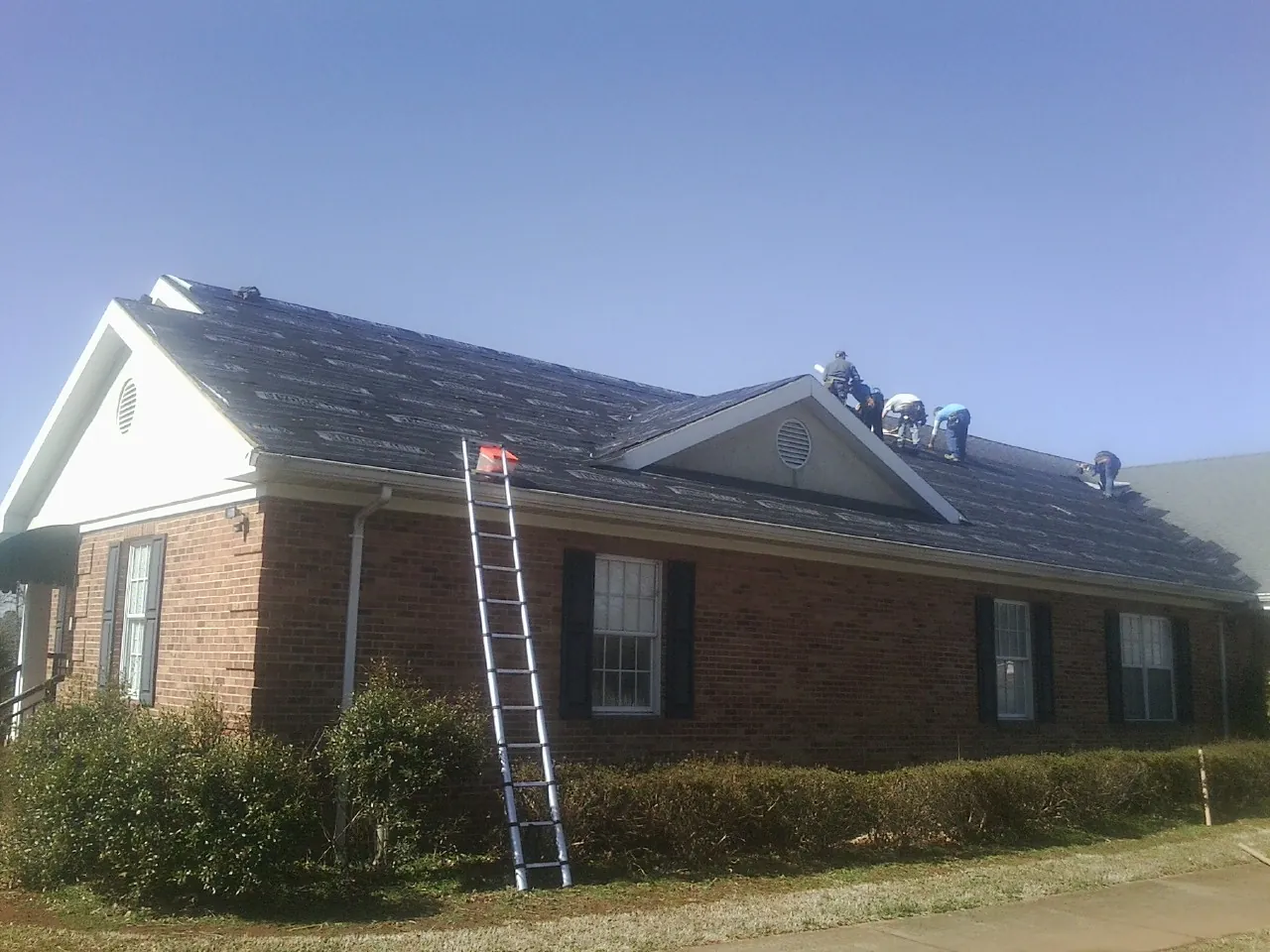 Crew tearing shingles off a brick ranch roof with a ladder set — Metal Roof Repair work by our crew in Hardyville