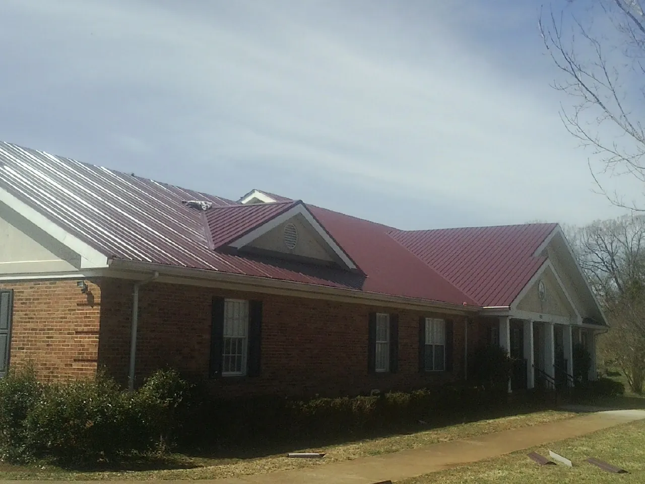 Red metal roof with gabled entries on a long brick building, from a Hail Damage Roof Repair job in Hardyville