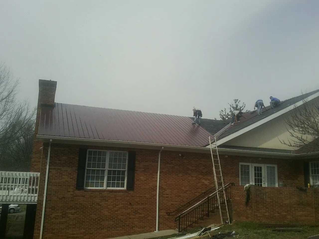 Crew setting red metal roofing panels on a brick home in Hardyville