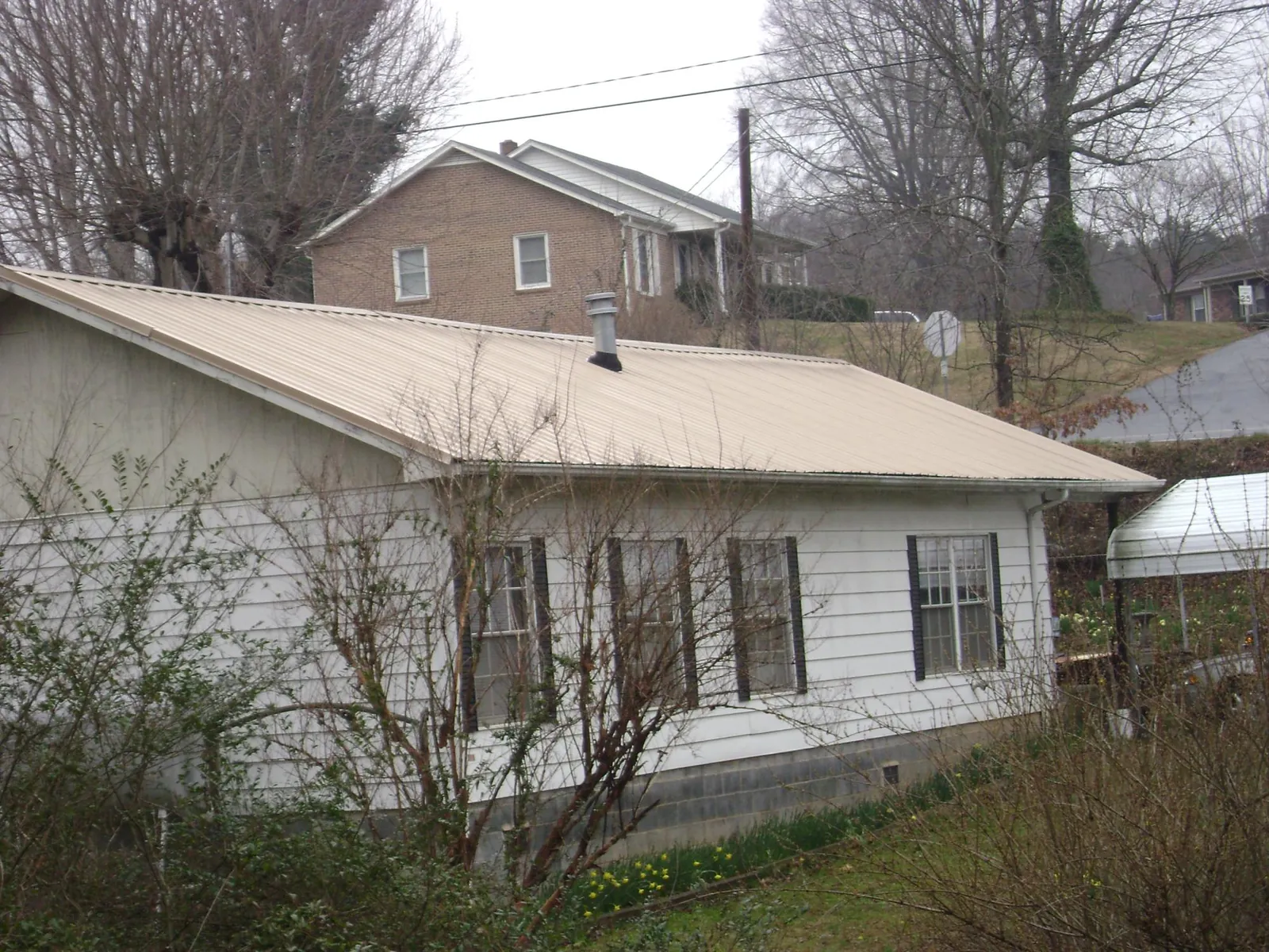 Tan metal roof on a white sided house set into a hillside — Commercial Roofing by Roofing Brothers in Hardyville
